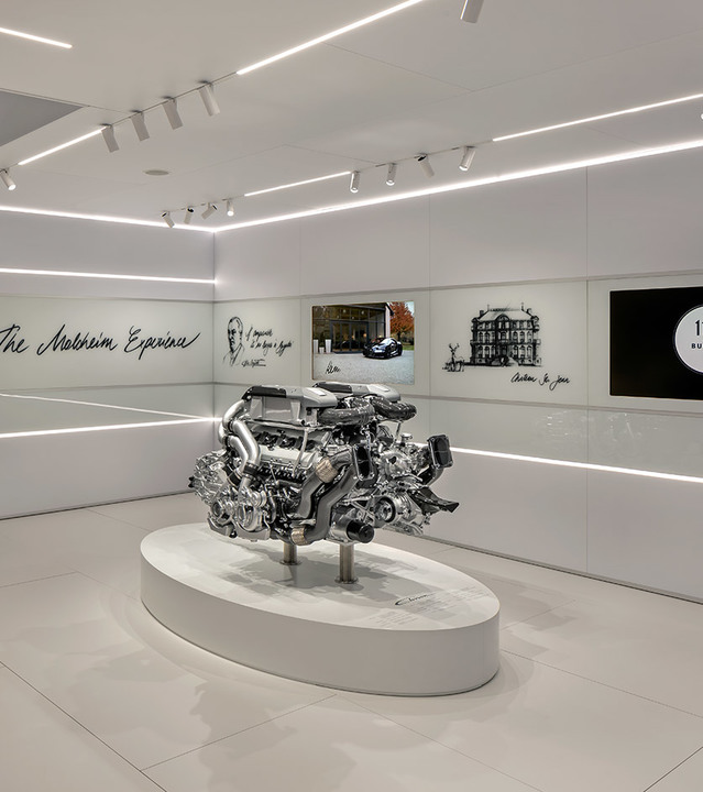 Showroom di lusso con illuminazione lineare a incasso e su binario Artemide che illumina un motore auto su piedistallo bianco