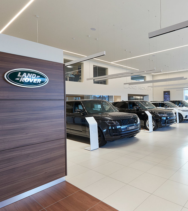 Land Rover showroom with linear LED ceiling lights illuminating a row of luxury SUVs on white tiled floor