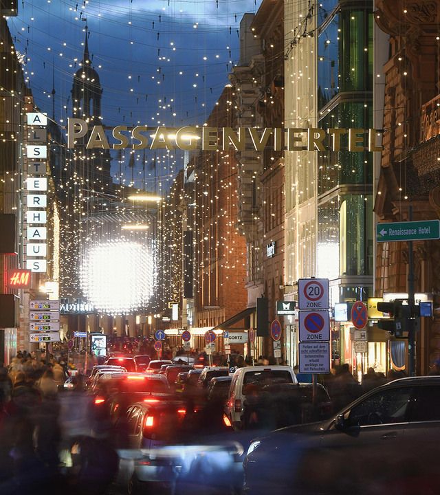 Via dello shopping Passagenviertel al crepuscolo, adornata con luci natalizie e un'insegna luminosa sopra il traffico intenso.