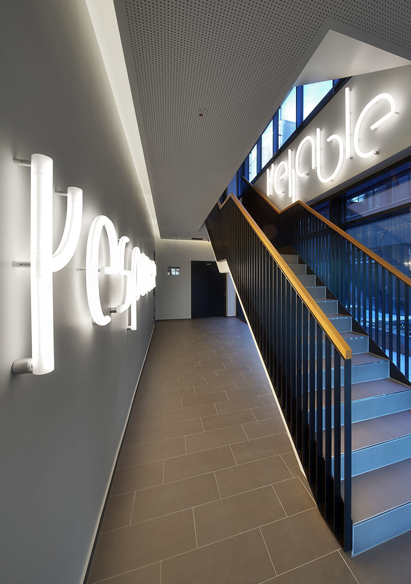 Corridoio moderno con insegne luminose 3D sulle pareti che formano 'people' e 'reliable', con luci a soffitto incassate e una scala.