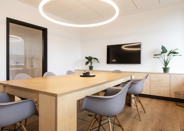 Modern meeting room with Artemide circular LED pendant light illuminating a wooden table surrounded by grey chairs.