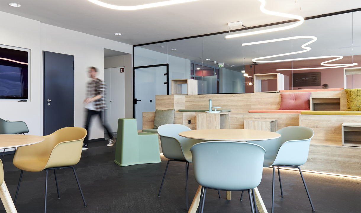 Modern office lounge with Artemide pendant light in organic shape, colorful chairs, round table, and glass partition wall.
