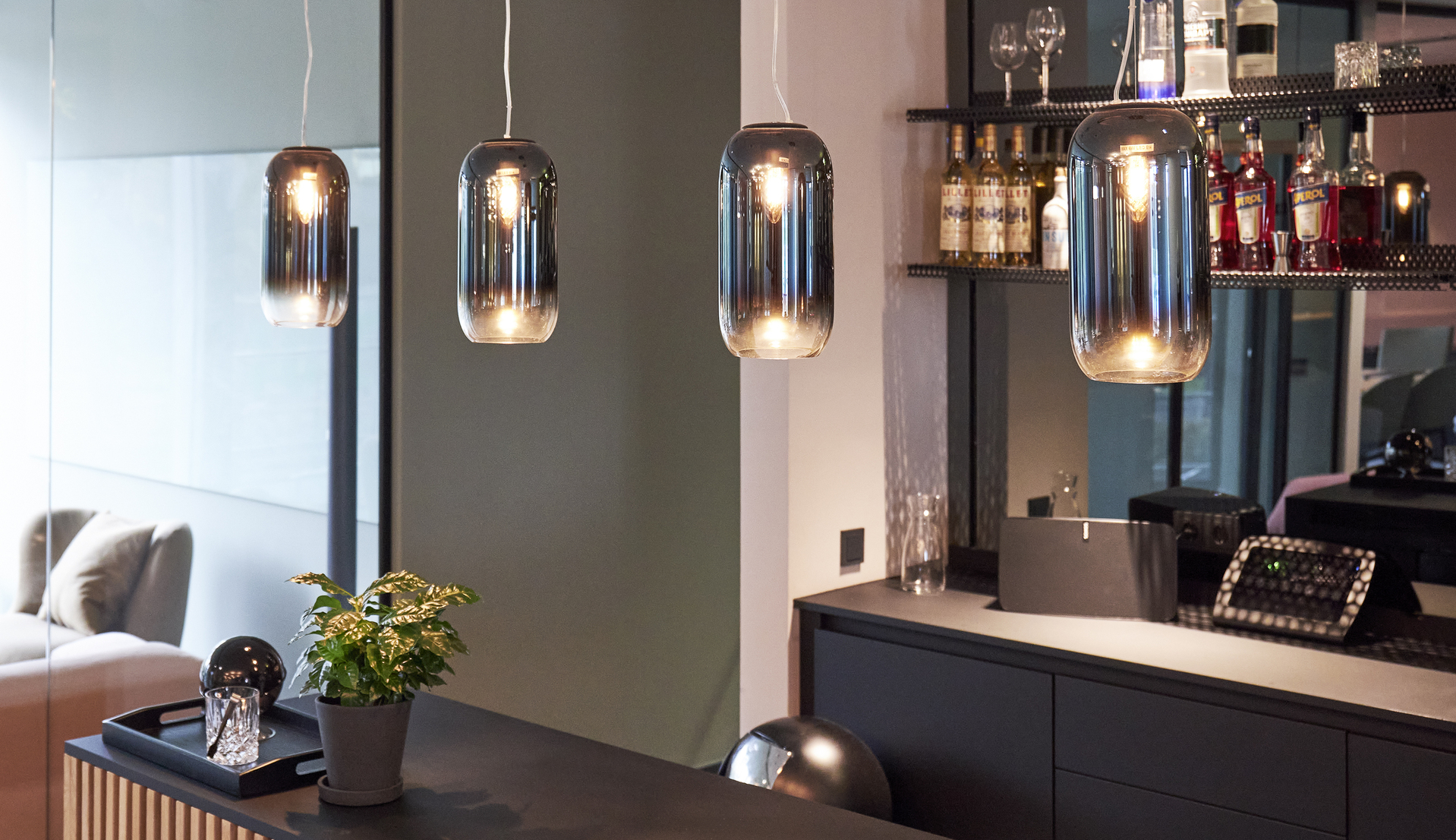 Three Artemide smoked glass pendant lamps hanging above a bar counter, creating elegant ambient lighting in a modern interior.