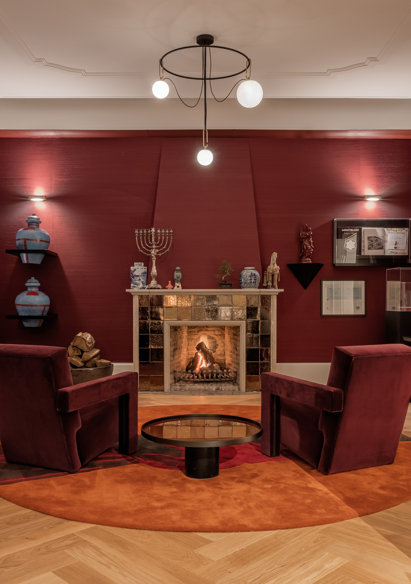 Cozy lounge with lit fireplace, two burgundy velvet armchairs, and an Artemide pendant lamp with three white globe shades on black frame
