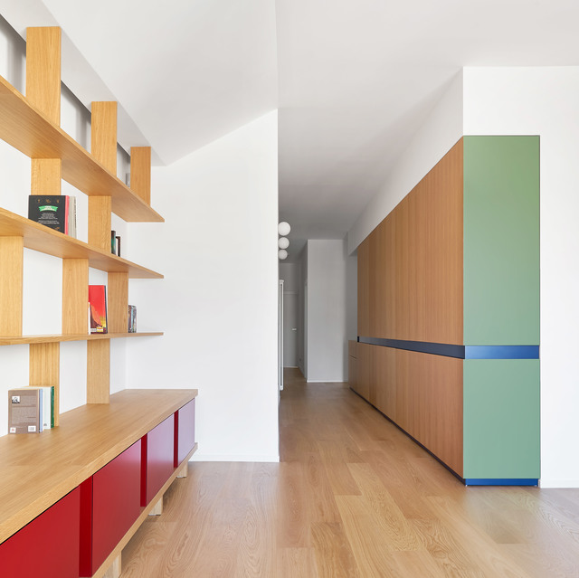 Interno moderno con scaffalature in legno, mobili colorati rossi e verdi e tre lampade a sospensione sferiche bianche che illuminano un corridoio.