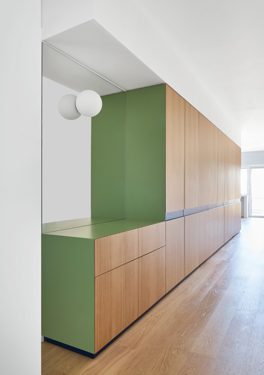 Lampada da parete sferica bianca Artemide montata su parete bianca accanto a mobili a muro in verde e legno in interno moderno