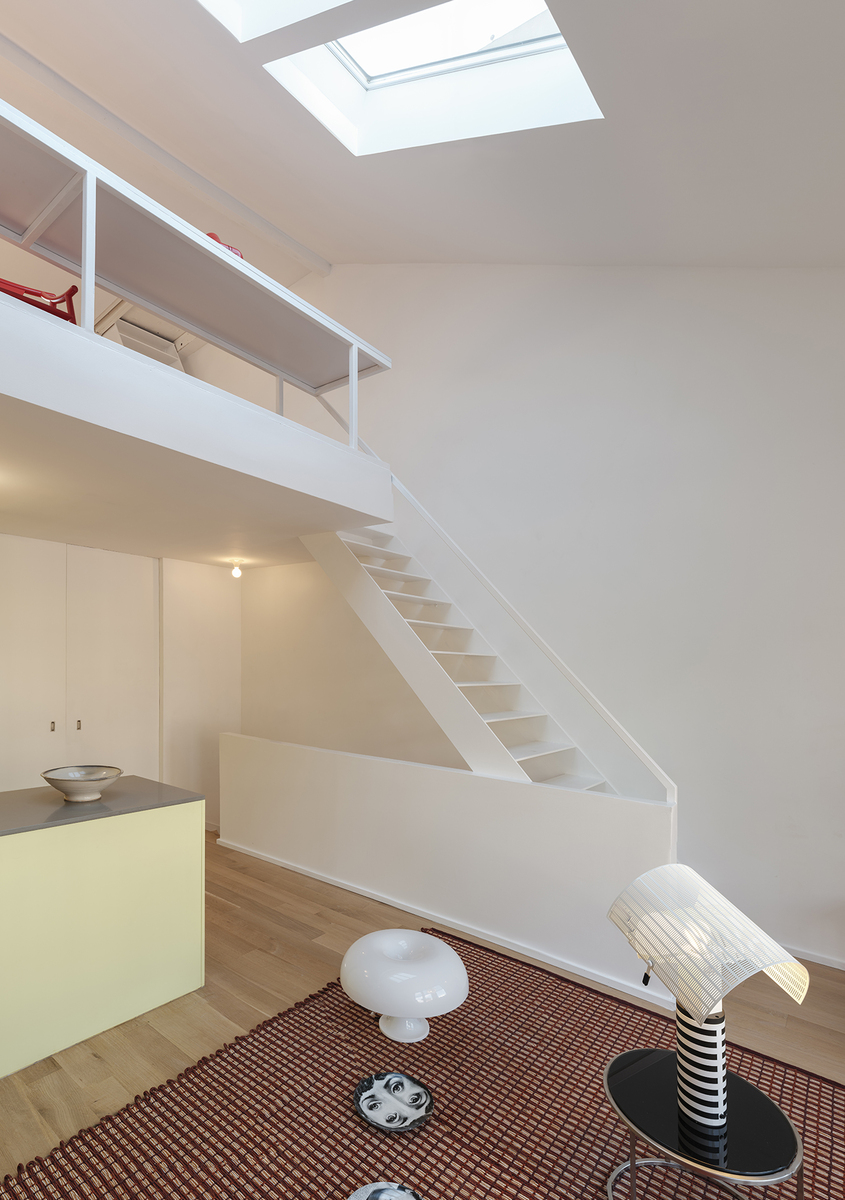 Interno duplex moderno con lampada da tavolo Artemide Nesso e lampada da terra Chiara su tappeto fantasia, scala bianca e lucernario sopra