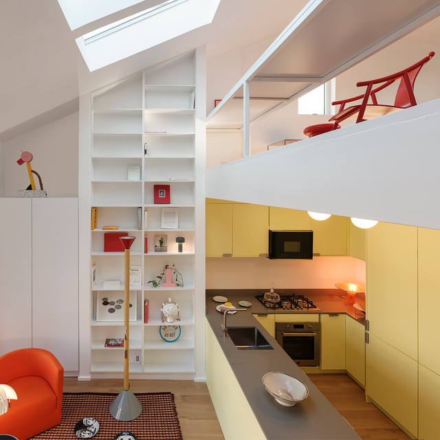 Cucina loft moderna con pensili gialli, lucernario, libreria bianca e lampada da terra Artemide con base grigia nel soggiorno