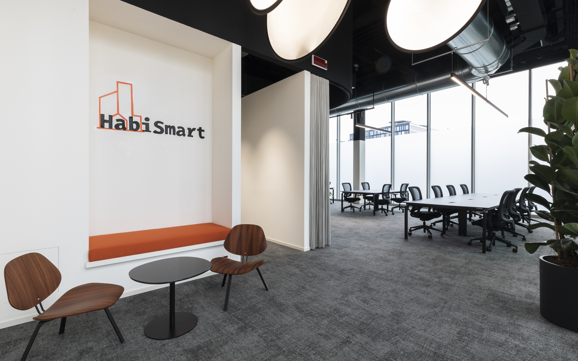 Ufficio HabiSmart con grandi lampade a sospensione rotonde, tavolo conferenze, area relax con sedie in legno e finestre a tutta altezza