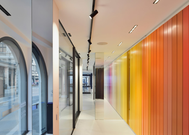 Corridoio moderno con faretti su binario Artemide neri a soffitto, che illuminano una parete a gradiente vivace in tonalità gialle, arancioni e rosse.