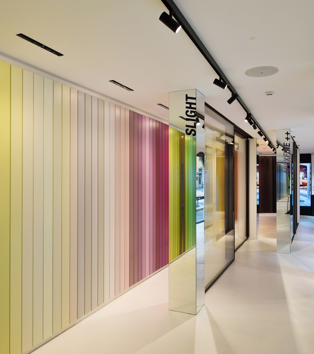 Corridoio showroom Artemide con faretti su binari neri che illuminano una parete a strisce colorate e colonne a specchio