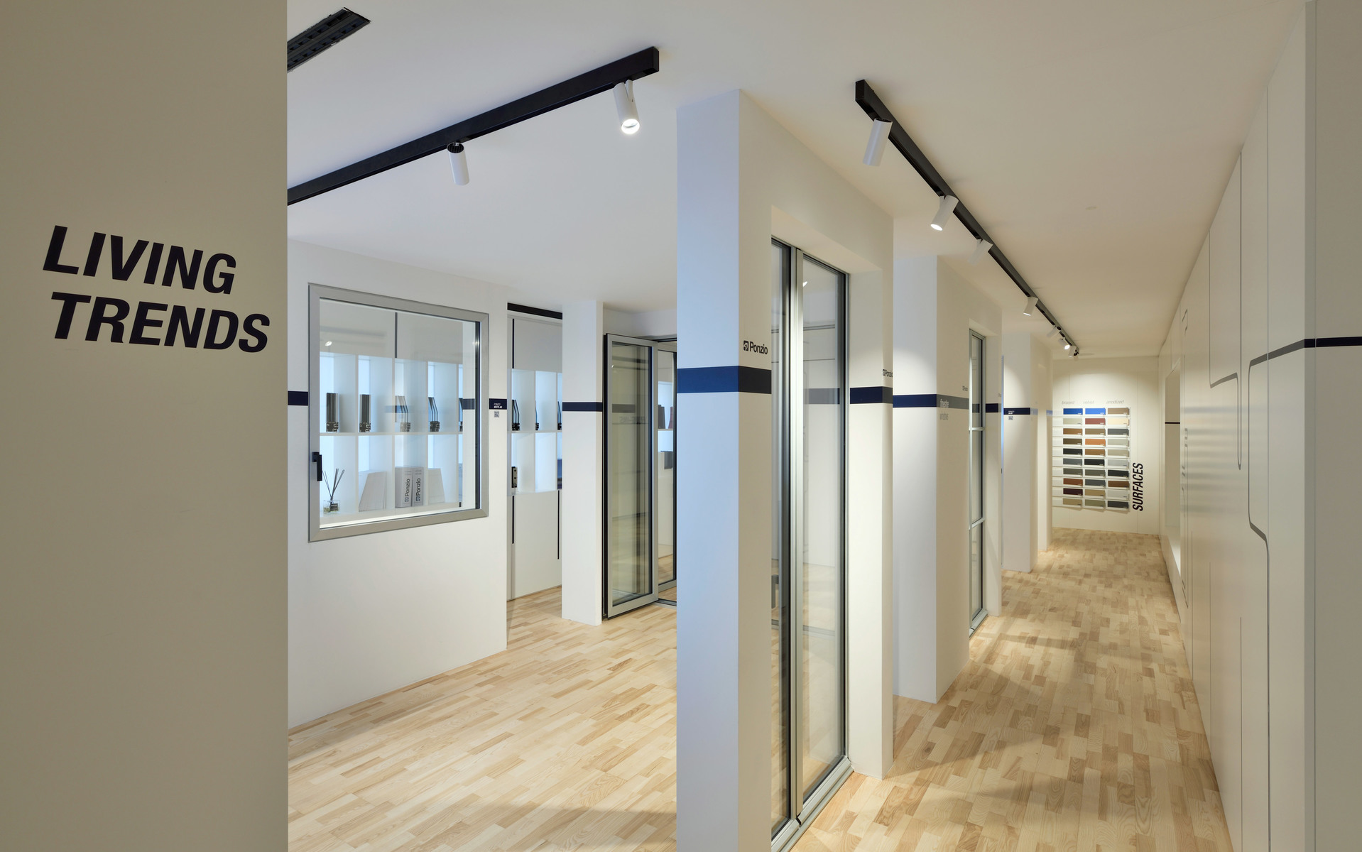 Corridoio di showroom moderno con insegna 'Living Trends', binari neri sul soffitto bianco e pavimento in legno chiaro.