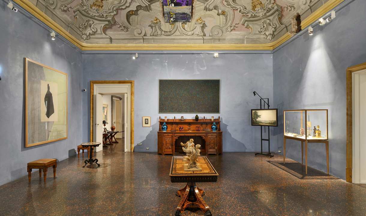 Elegante sala museale con soffitto affrescato, pareti blu, mobili antichi, opere d'arte, vetrine e faretti Artemide che illuminano le esposizioni.