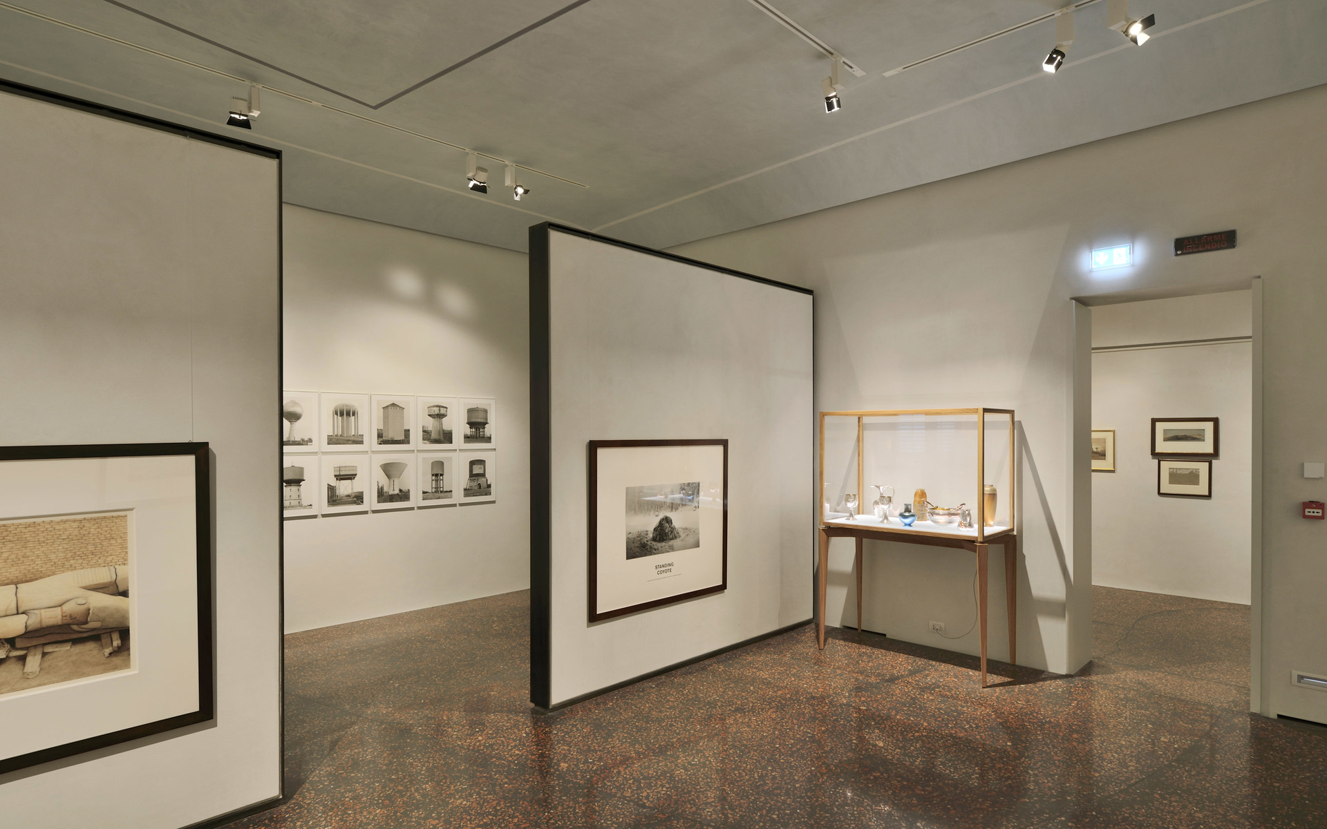 Galleria museale con faretti da soffitto Artemide che illuminano opere incorniciate su pareti bianche e una teca in vetro con oggetti.