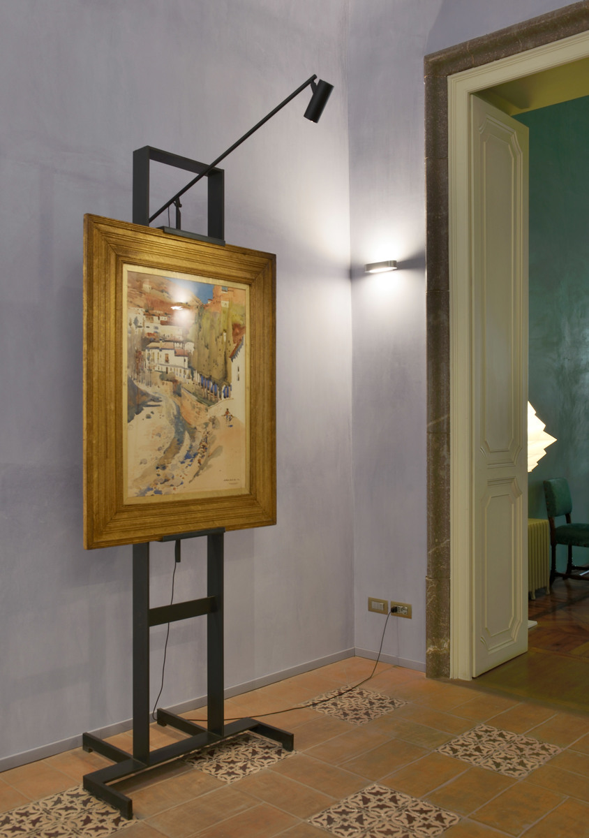 Faretto orientabile nero Artemide su cavalletto che illumina un dipinto incorniciato in un interno classico con pavimento in cotto