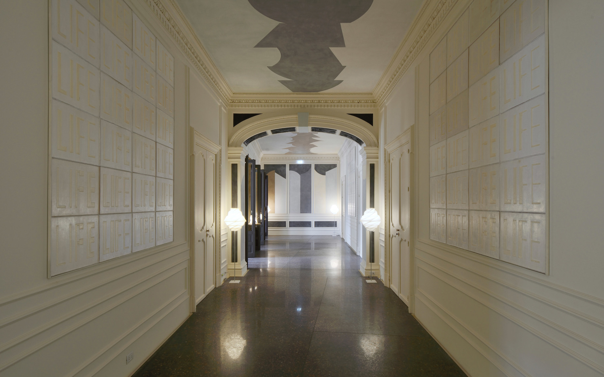 Corridoio elegante con architettura classica, illuminato da due lampade da terra sferiche bianche ai lati di un grande arco con pavimento in marmo scuro.