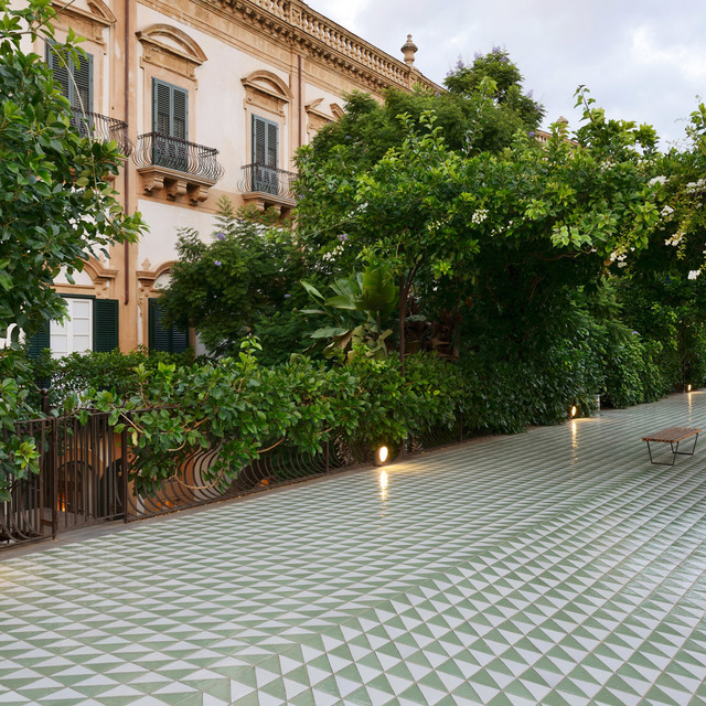Cortile esterno di una villa storica con pavimento geometrico verde-bianco, giardino rigoglioso e luci a terra Artemide che illuminano il percorso.