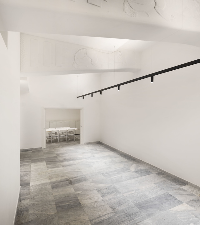 Minimalist white corridor with grey marble floor, black track lighting rail with spotlights on ceiling, leading to a bright meeting room.