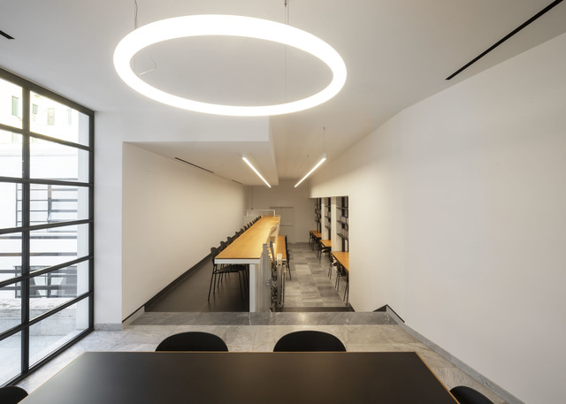 Artemide Alphabet of Light circular pendant illuminates a modern meeting room with long wooden tables and linear ceiling lights.