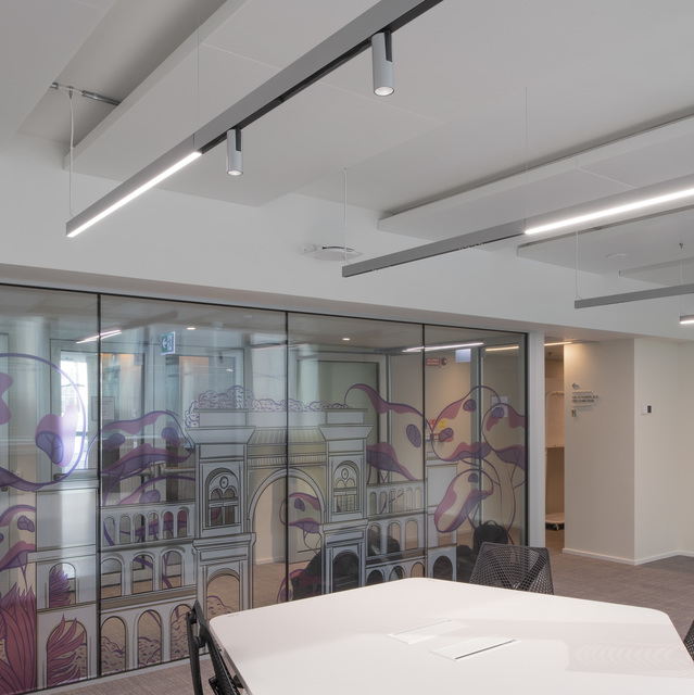 Modern office meeting room with Artemide linear LED ceiling lights and track spotlights, glass partition wall with decorative mural artwork.