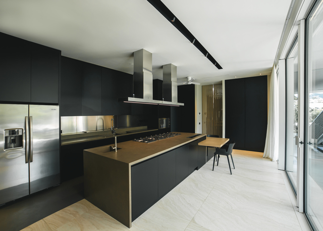 Modern kitchen with black cabinetry, island cooktop, stainless steel appliances, and Artemide track lighting system on white ceiling.