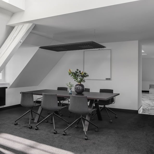 Conference room with dark table, six chairs, and a rectangular black perforated ceiling light fixture above, whiteboard on wall.