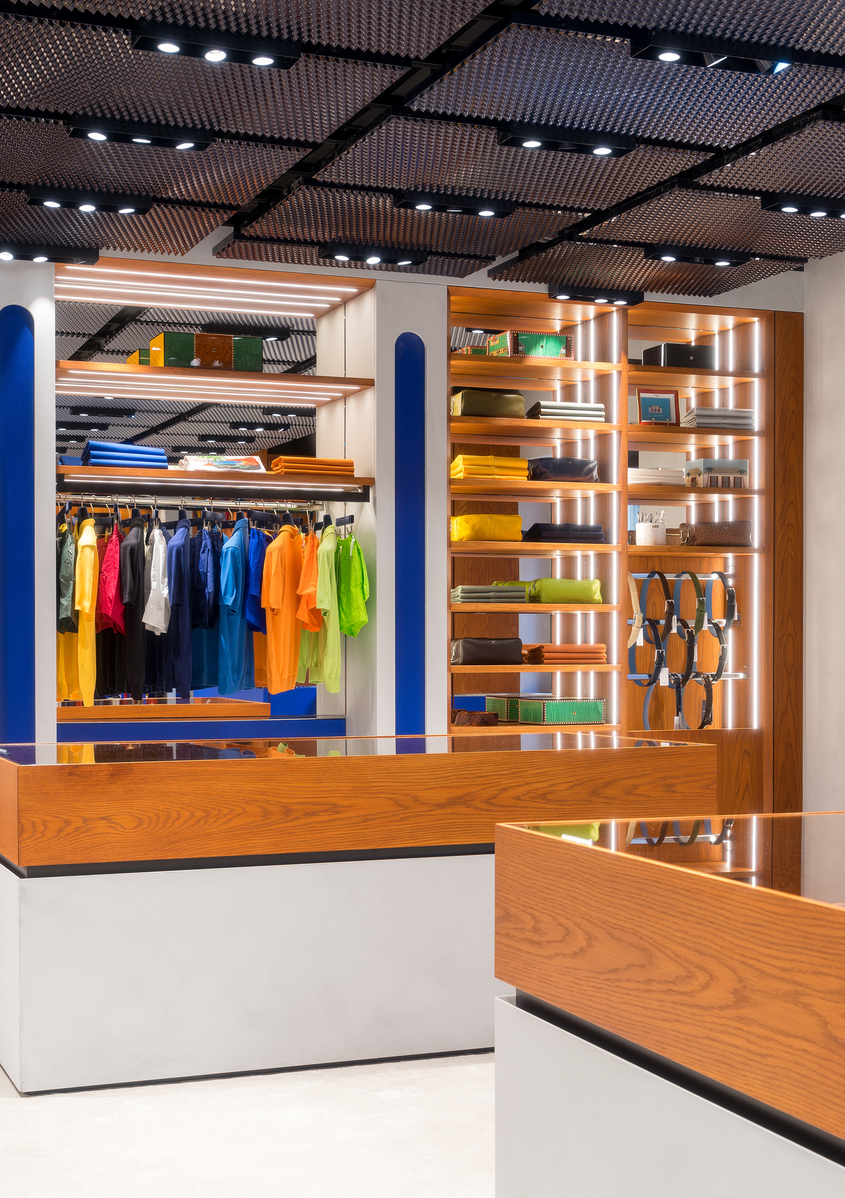 Interno di negozio moderno con faretti da incasso Artemide che illuminano appendiabiti colorati e scaffalature in legno con luce calda.
