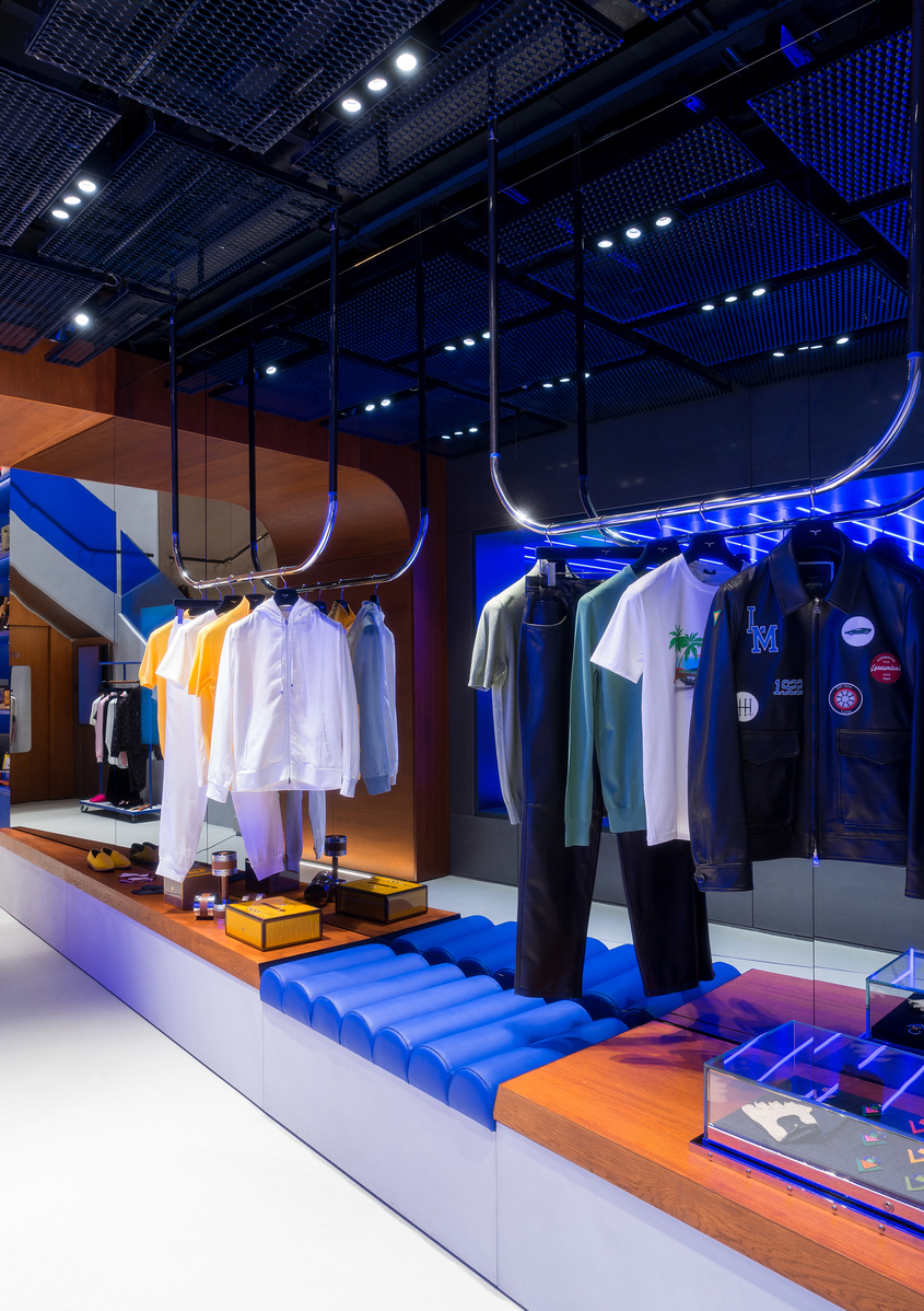 Negozio moderno con faretti da incasso Artemide e illuminazione al neon blu che illumina espositori di abbigliamento su appendiabiti.