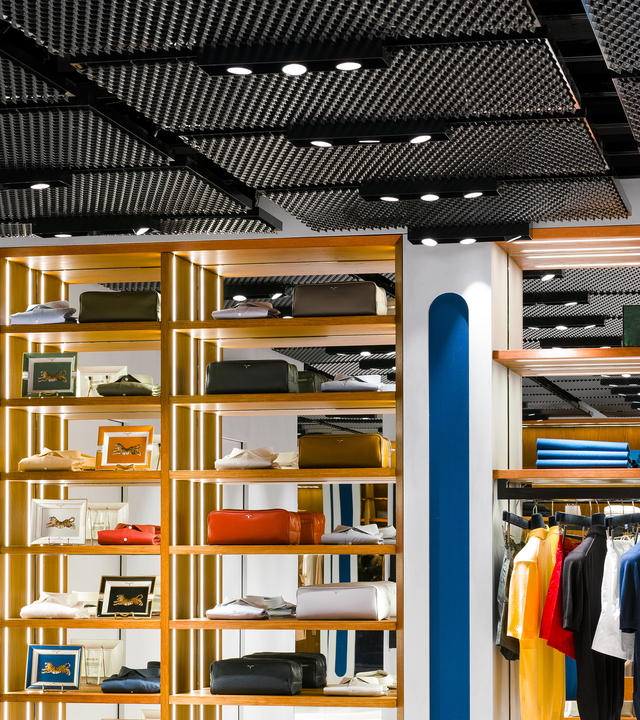 Interno di negozio con faretti a incasso su soffitto nero texturizzato che illuminano scaffali in legno con articoli di lusso e abbigliamento.