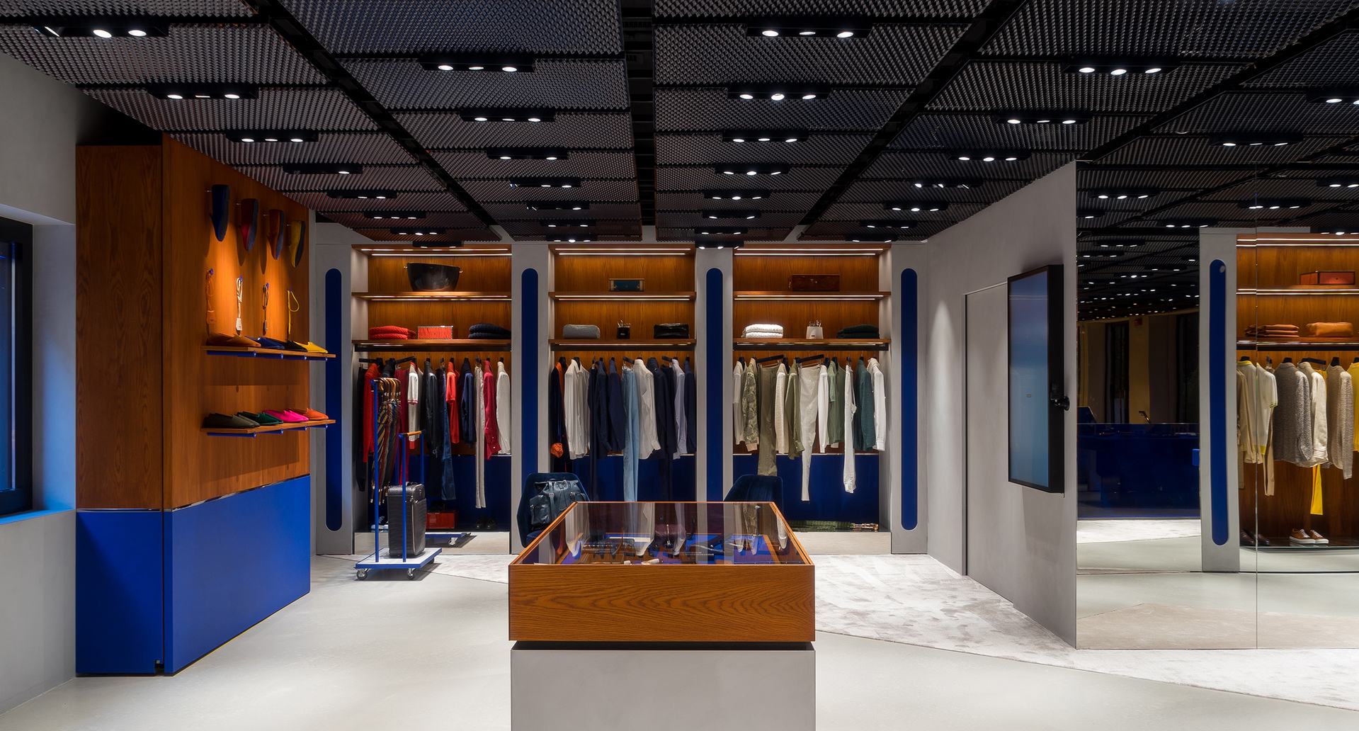Interno di negozio moderno con faretti da incasso Artemide a soffitto che illuminano espositori di abbigliamento, scaffalature in legno e una vetrina centrale.