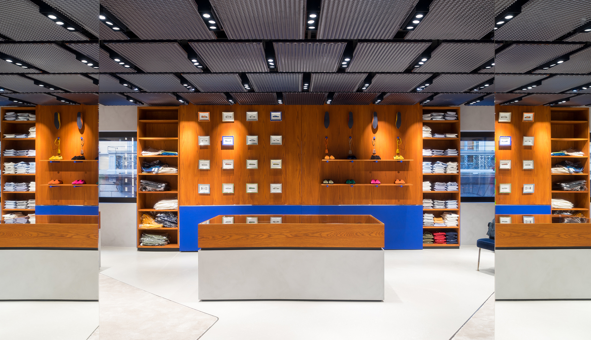 Interno di negozio moderno con scaffalature in legno caldo, accenti blu e faretti da incasso Artemide che illuminano i prodotti esposti su griglia a soffitto.