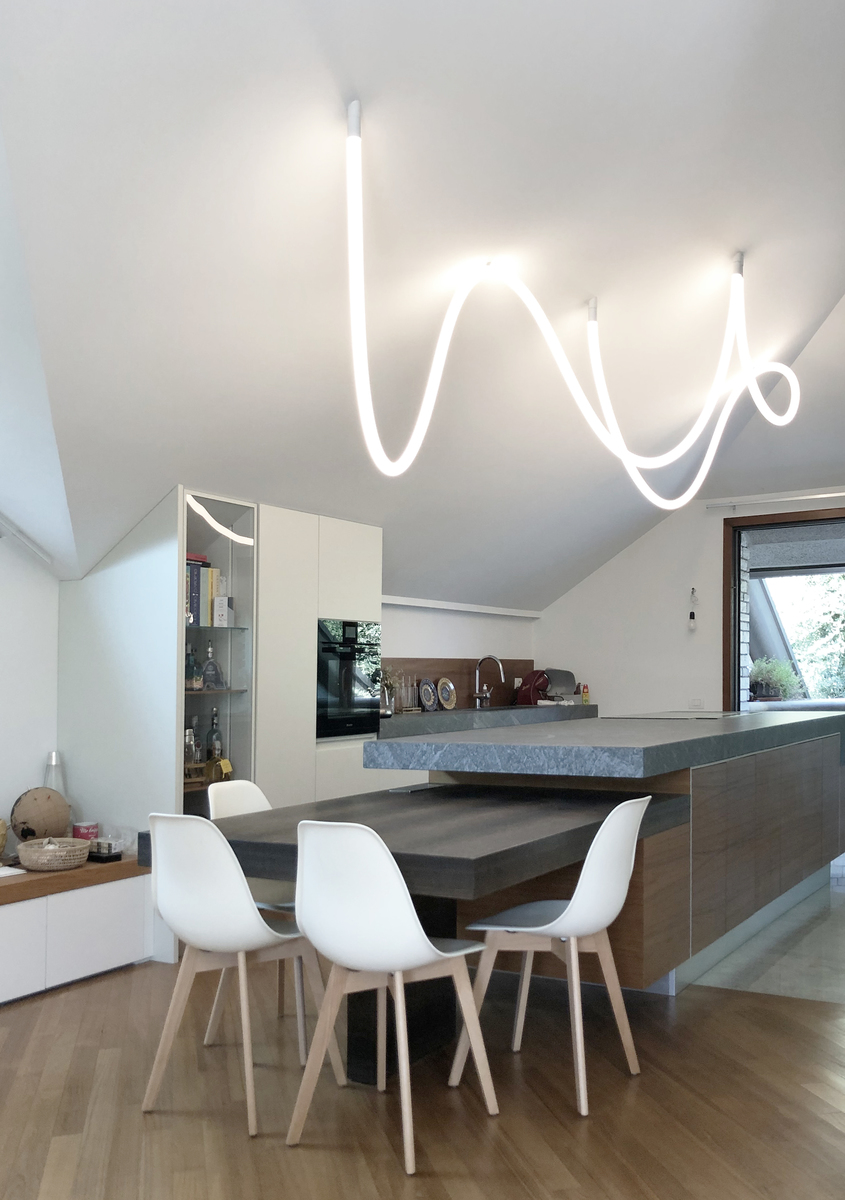 Artemide flexible LED tube light in a wavy shape suspended from ceiling over a modern kitchen island with white dining chairs
