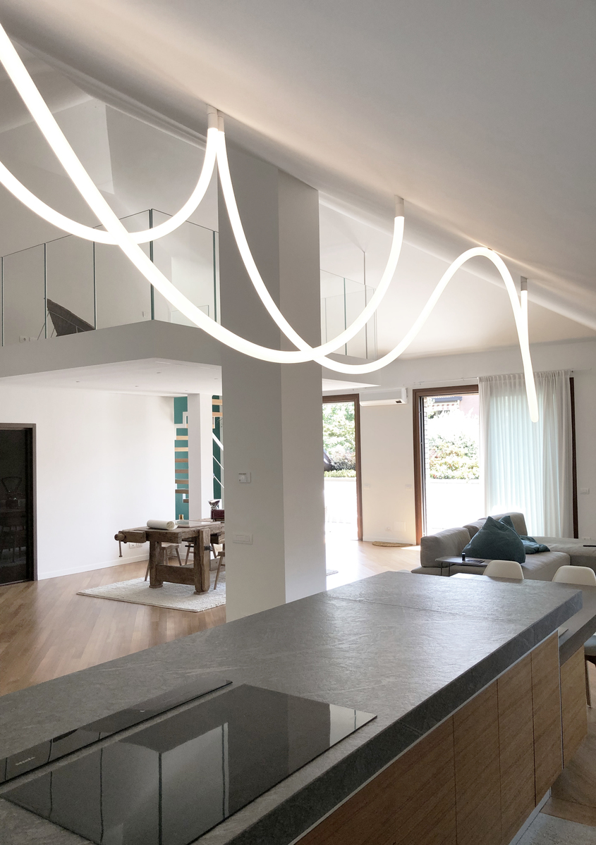 Artemide flexible LED light tubes draped in flowing curves across a modern open-plan living space with kitchen island