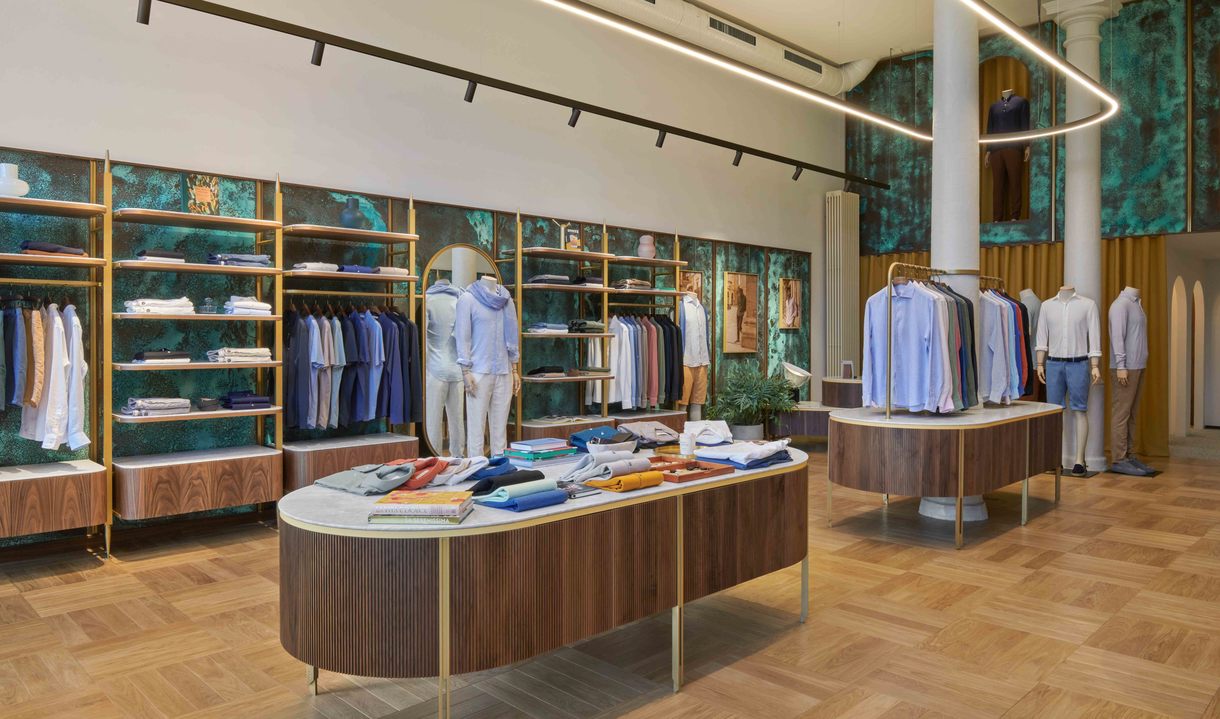 Elegante boutique maschile con lampada a sospensione ad anello LED circolare Artemide che illumina tavoli espositivi in noce e scaffali dorati