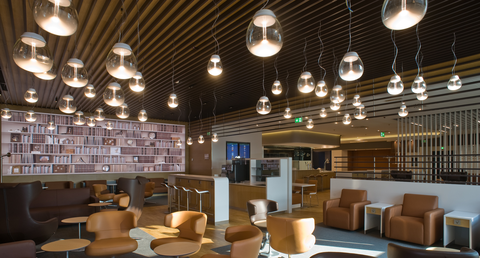 Interno di una lounge con più lampade a sospensione Artemide Muse in vetro trasparente a diverse altezze sopra l'area salotto.