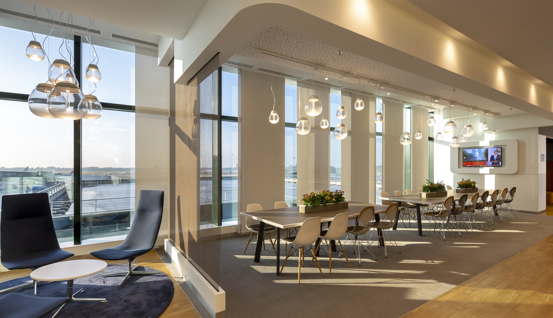 Lounge ufficio moderno con lampade a sospensione Artemide con diffusori in vetro, finestre a tutta altezza, zona pranzo e arredi contemporanei.