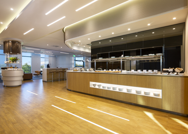 Area buffet di un ristorante moderno con luci a incasso nel soffitto e strisce LED lineari che illuminano banconi in legno caldo e pavimento.
