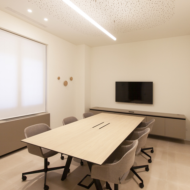 Modern meeting room with linear ceiling LED light over a light wood conference table surrounded by grey chairs on casters
