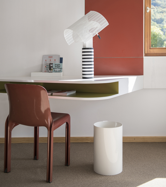 Artemide Shogun table lamp with striped base and tilted white shade on a floating desk beside a brown chair