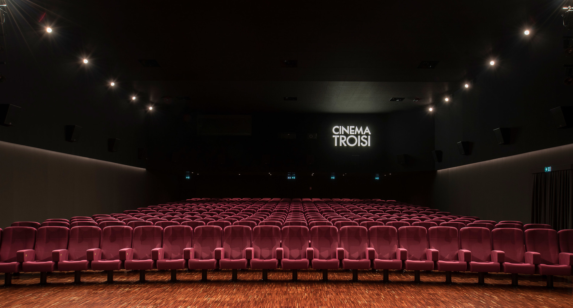 Cinema Troisi auditorium with rows of red velvet seats, dark ceiling with recessed spotlights illuminating the empty hall.