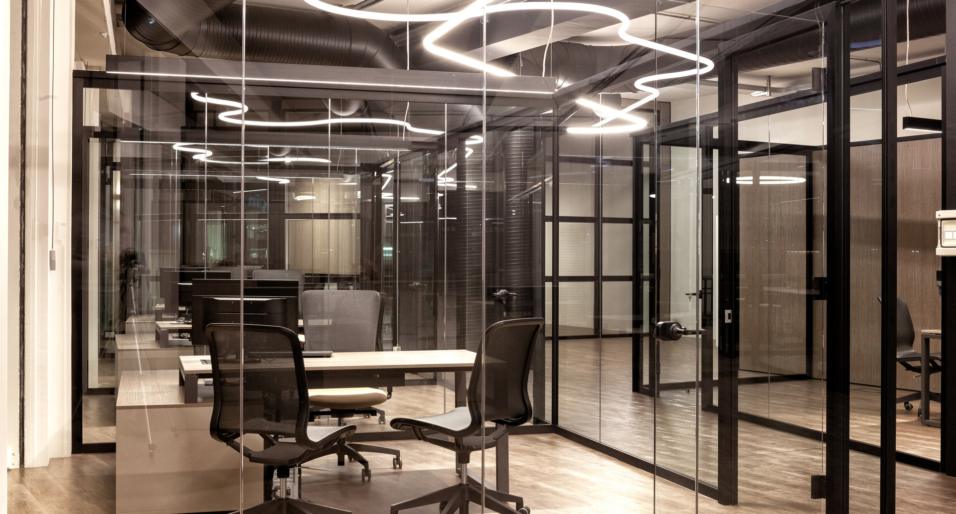 Modern office with glass partitions and Artemide pendant lights in organic shapes illuminating workstations with dark ergonomic chairs.