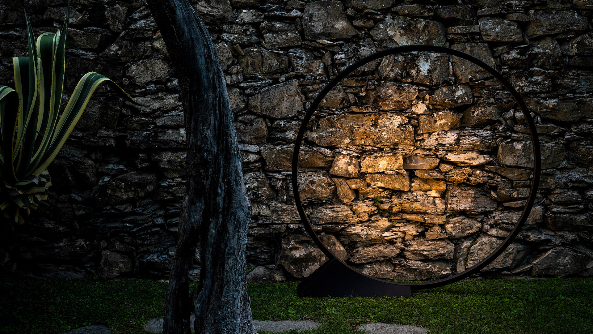 Lampada a sospensione Artemide 'O' Elemental: anello circolare in metallo scuro con rami fioriti, progettata da Workshop Elemental e Alejandro Aravena