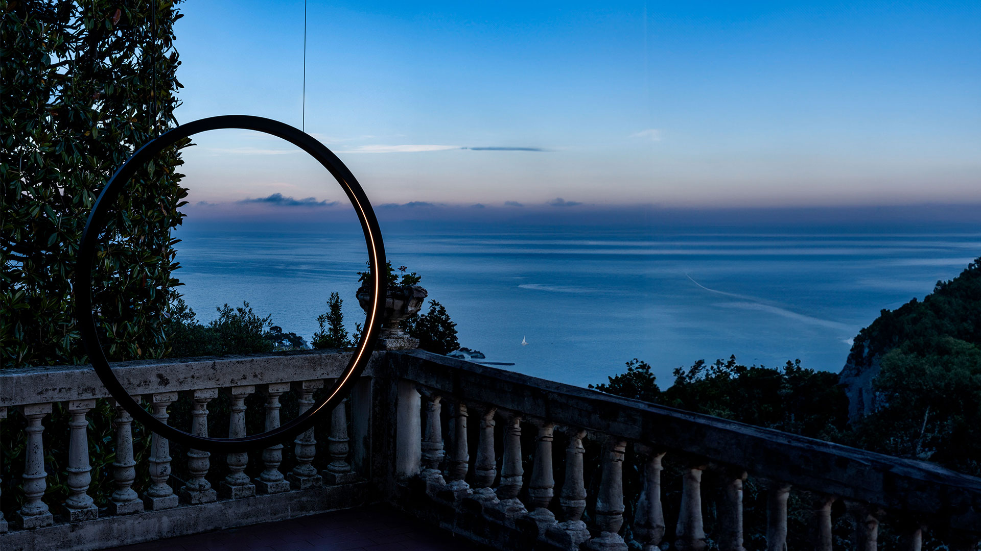 Due lampade da terra outdoor Artemide 'O' con anelli LED circolari in finitura scura, posizionate accanto a una piscina al crepuscolo