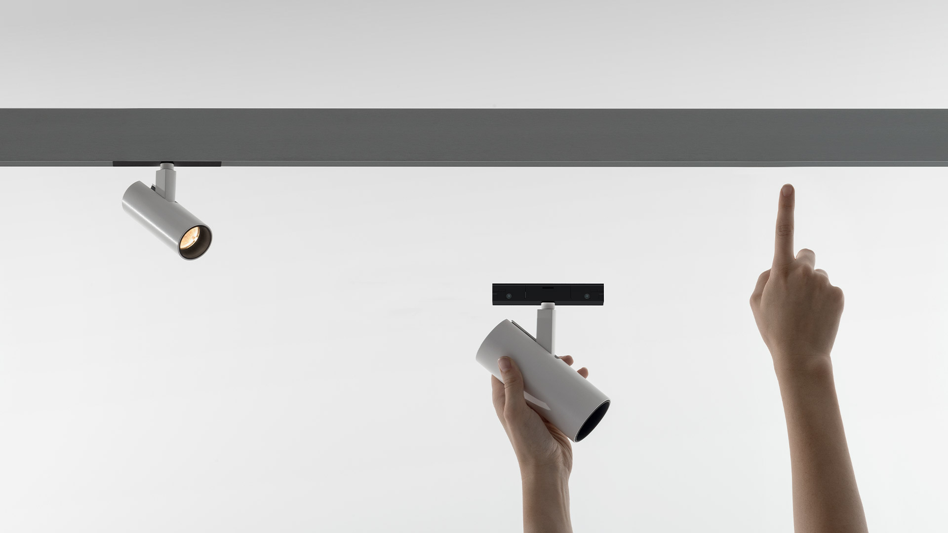 Ufficio moderno con illuminazione su binario magnetico Artemide A.24 su soffitto in cemento a vista, pareti in vetro, pavimento a strisce blu e modelli architettonici esposti.