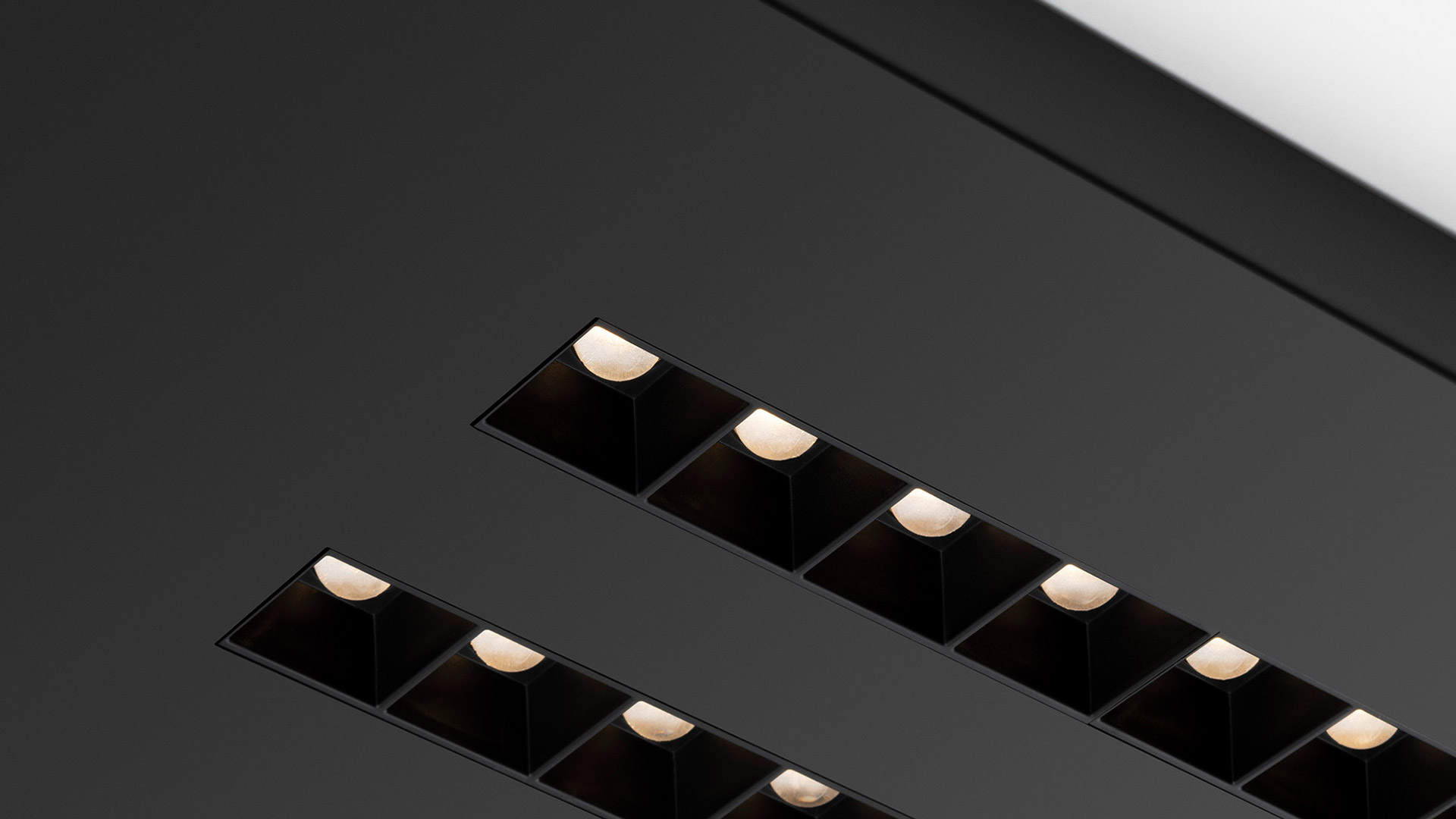 Due apparecchi da incasso lineari a soffitto A.39 Refractive Square di Artemide, con moduli quadrati neri multipli che emettono luce bianca calda