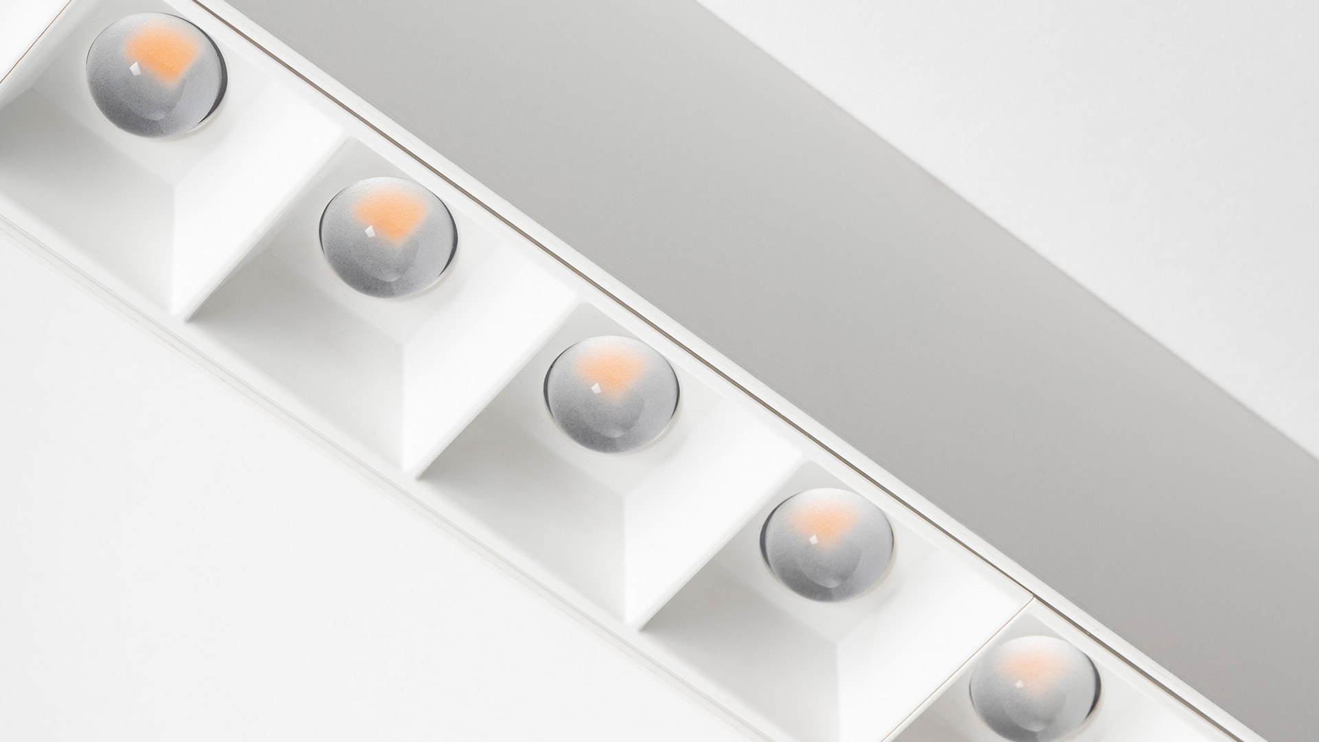 Showroom moderno con luci da soffitto incassate Artemide A.39 e strisce LED lineari che illuminano piedistalli espositivi scuri su pavimento curvo