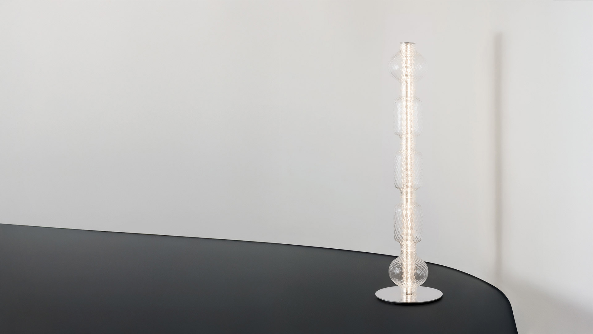 Artemide Alambicco horizontal pendant lamp: elongated clear textured glass body with four connected spherical bulges, warm LED light