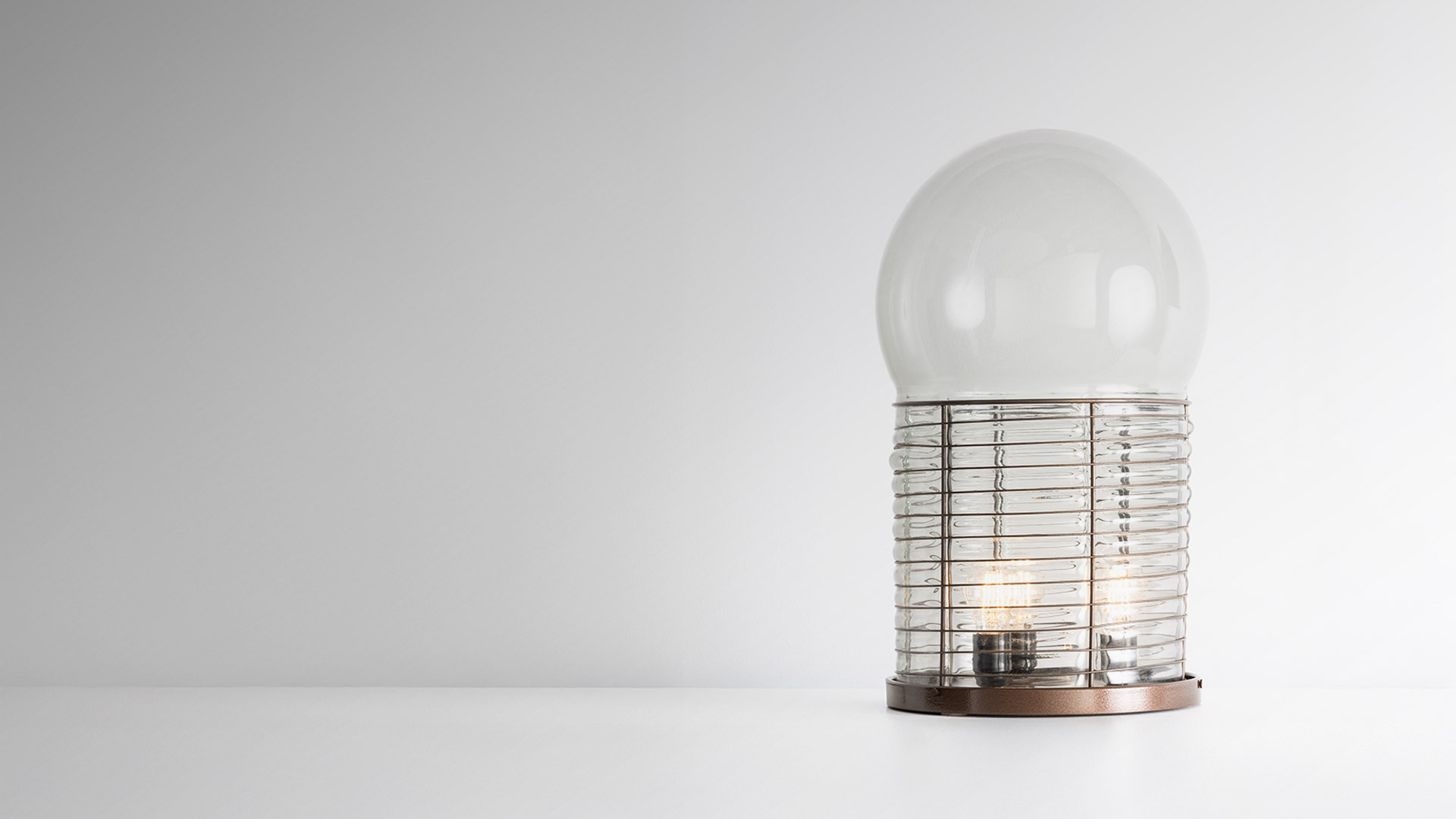 Lampada da tavolo Artemide Alcinoo: sfera in vetro trasparente su base cilindrica costolata con lampadine a vista, emette luce ambiente blu soffusa