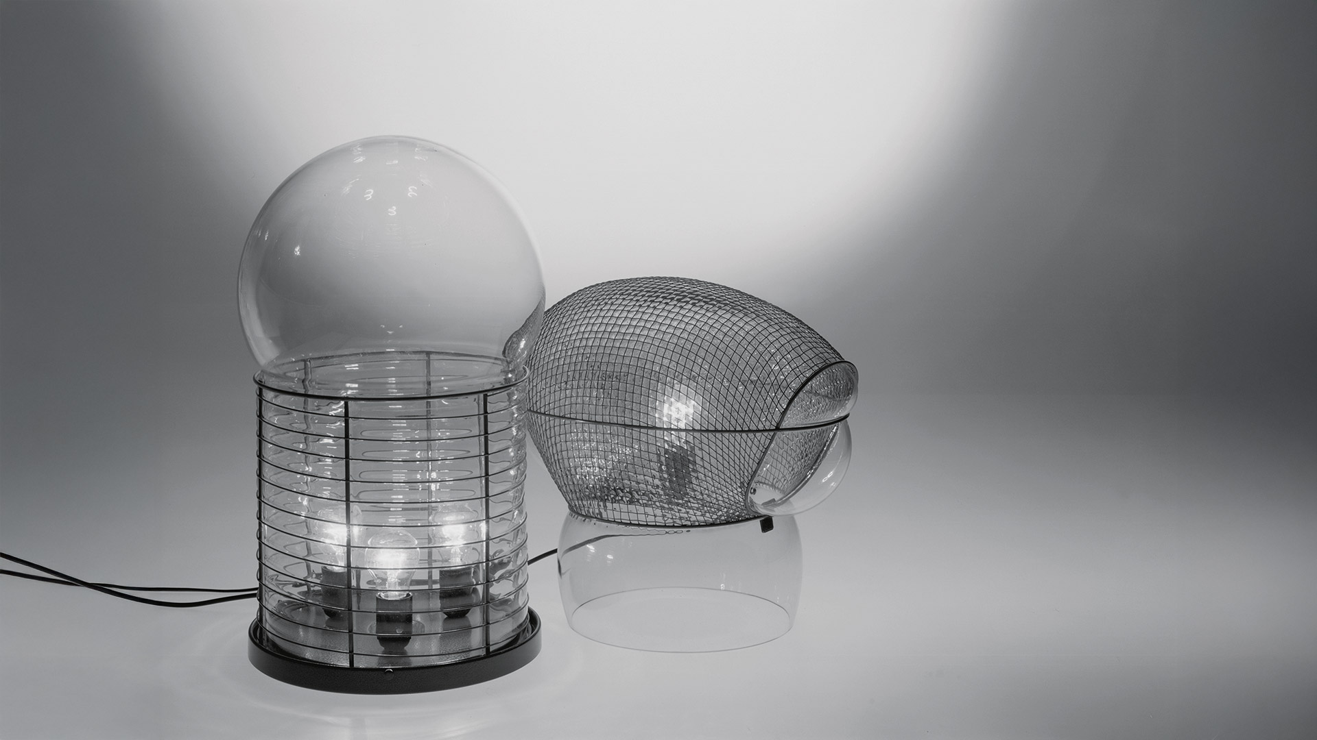 Lampada da tavolo Artemide Alcinoo con diffusore a globo in vetro trasparente su struttura cilindrica a gabbia metallica nervata con base in rame