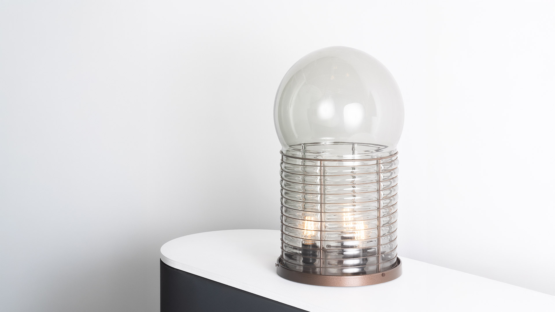Due dettagli della lampada Artemide Alcinoo: sinistra gabbia metallica nervata cromata con bulbo a globo, destra base in rame con diffusore in vetro nervato